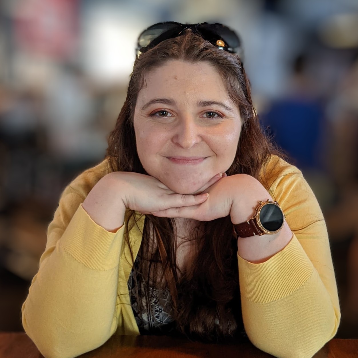 A photo of Abby wearing a yellow cardigan and smiling with her chin rested on her hands.